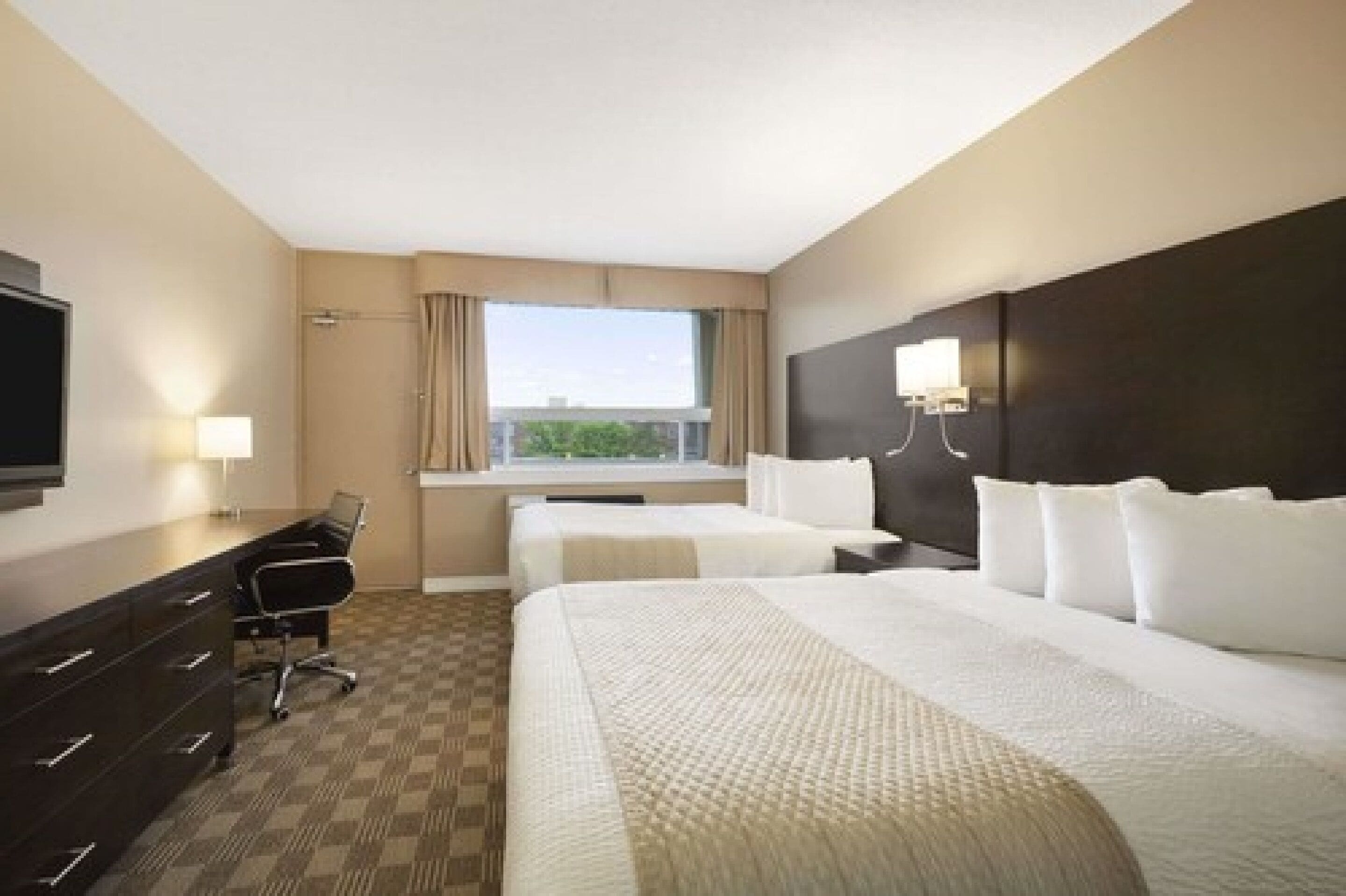 A hotel room with two beds, a desk, a chair, a TV, and a window with curtains.
