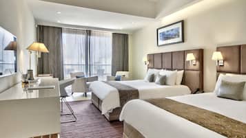 A hotel room with two beds, a desk, a chair, and a large window with curtains.