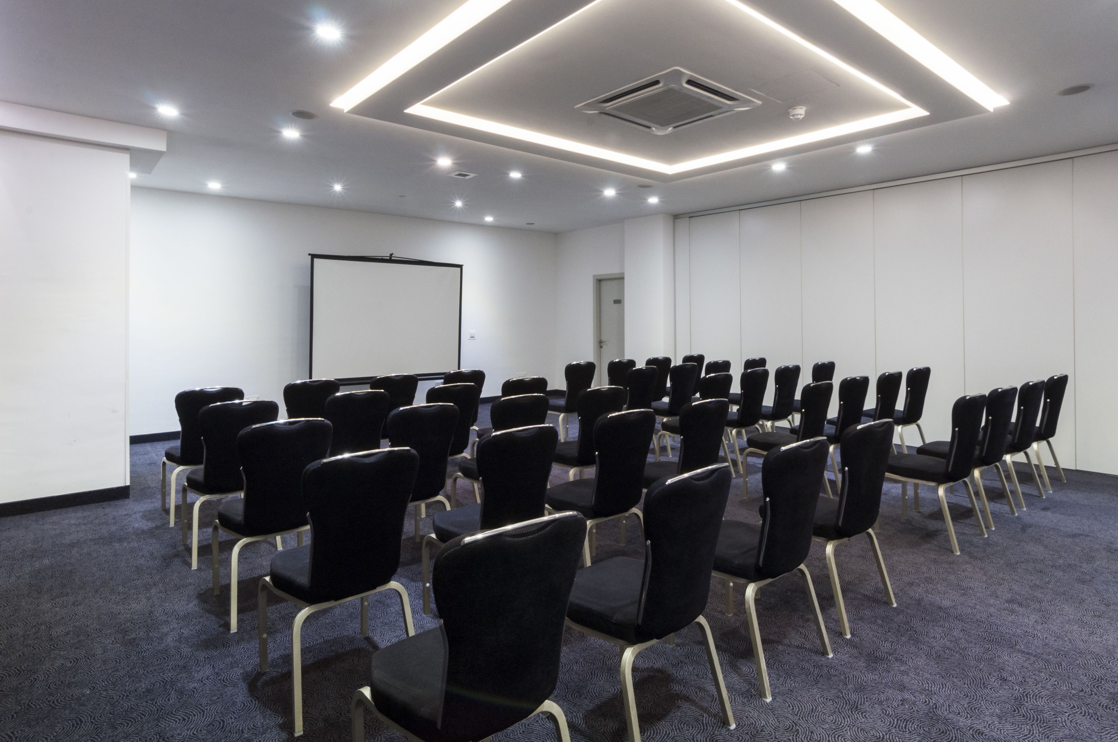 A conference room with rows of black chairs, a whiteboard, and recessed ceiling lighting.