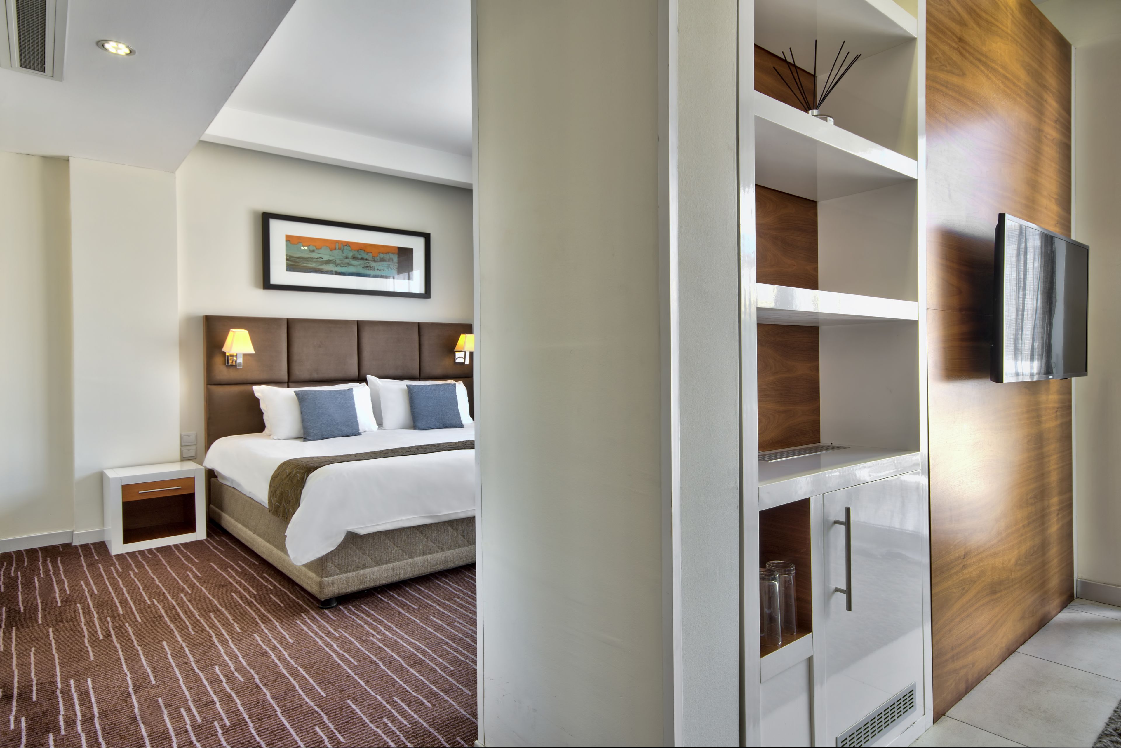 Habitación de hotel con cama, mesitas de noche, televisión y estanterías empotradas.