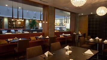 A modern restaurant with wooden accents, large windows, and a central dining area with tables set for guests.
