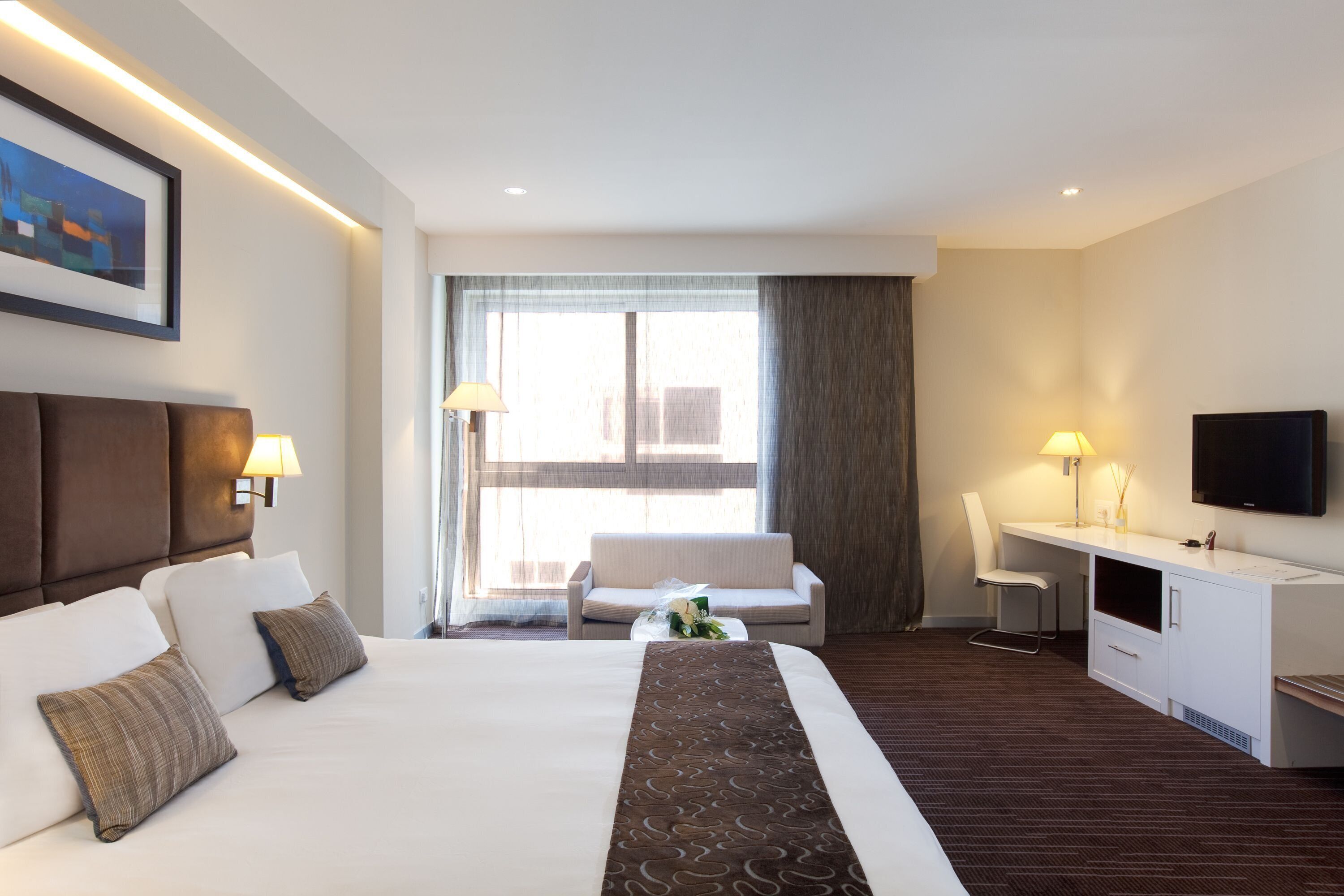 Een hotelkamer met een groot bed, een bureau, een stoel, een televisie en een raam met gordijnen.