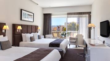 A hotel room with two beds, a desk, a chair, a TV, and a large window with a city view.