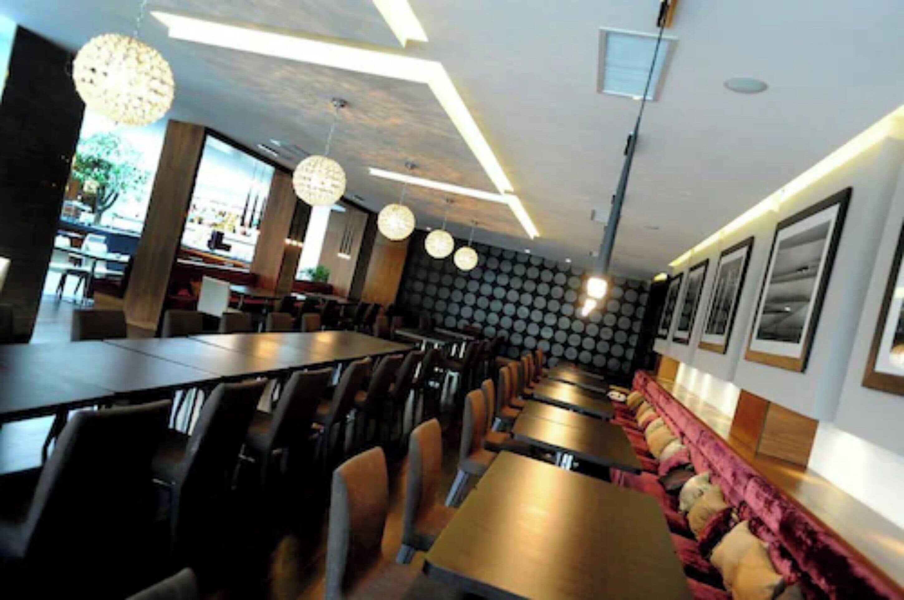 A modern restaurant interior with long tables, chairs, and hanging pendant lights.