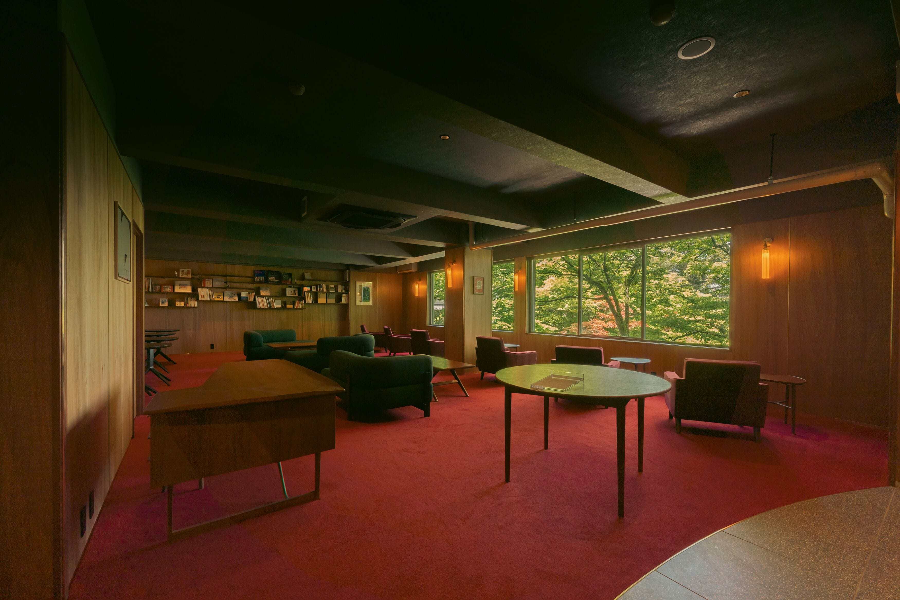 A spacious room with a red carpet, multiple seating areas, and large windows offering a view of trees.