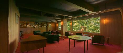 A spacious room with a red carpet, multiple seating areas, and large windows offering a view of trees.