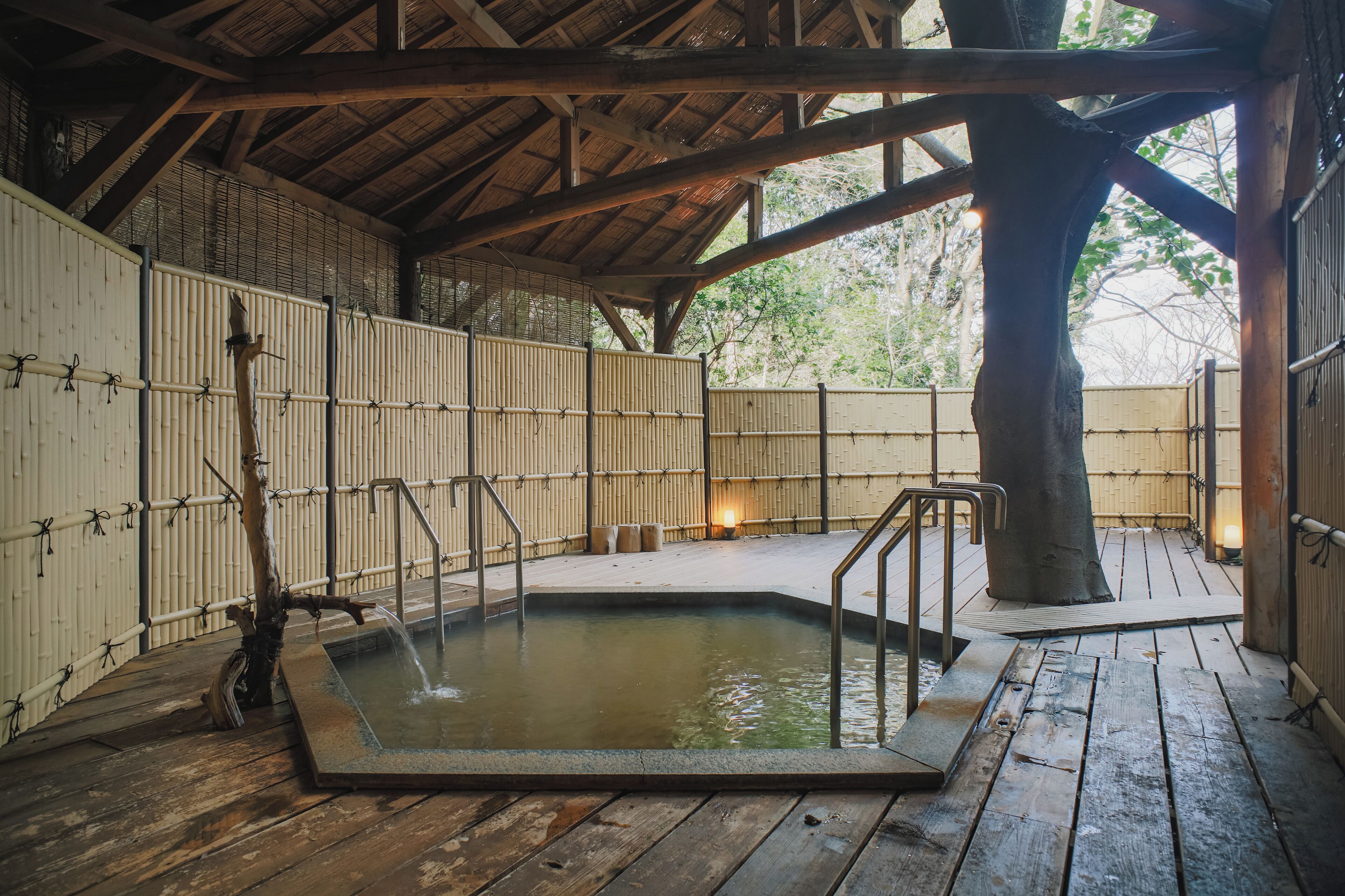 A traditional Japanese onsen with a wooden deck, a hot spring bath, and bamboo walls.