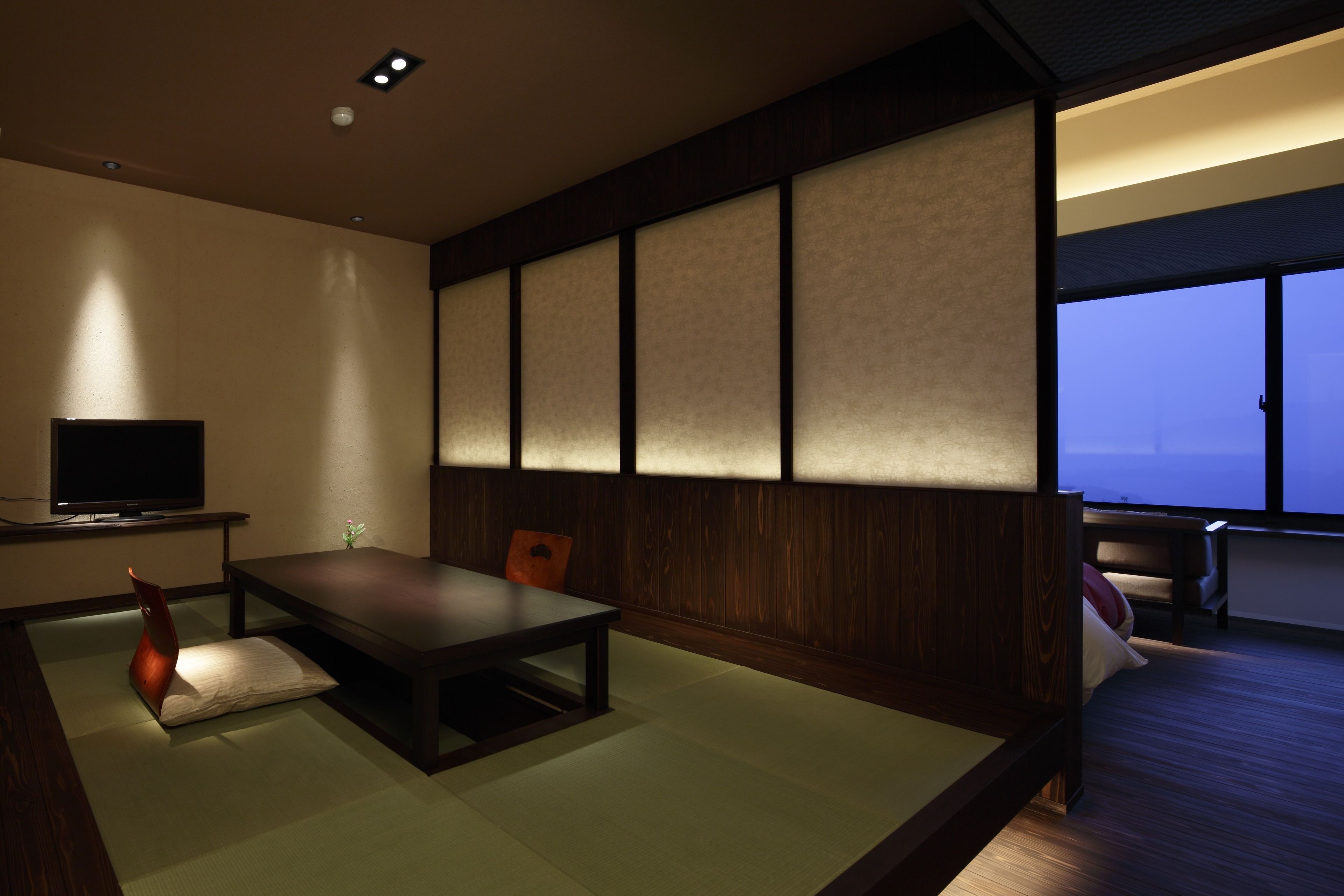 Ein traditioneller japanischer Raum mit Tatami-Boden, einem niedrigen Tisch, einem Fernseher und Schiebetüren.