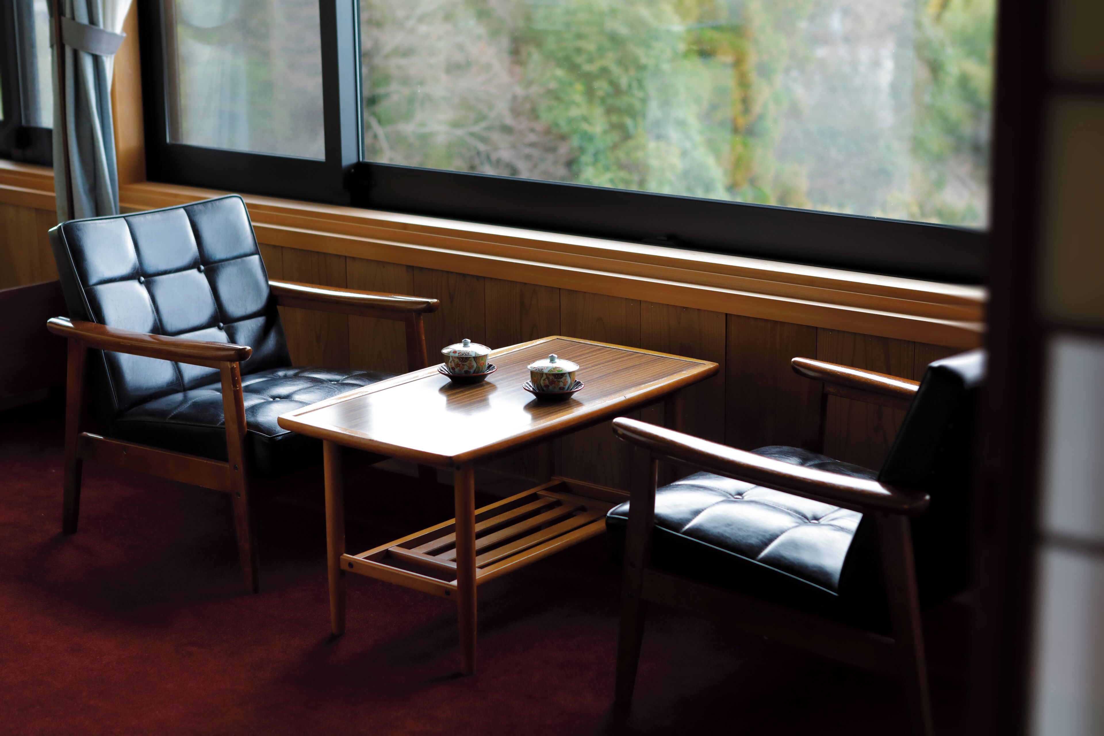Une pièce comprenant un banc en bois, deux fauteuils en cuir et une petite table sur laquelle se trouvent une théière et des tasses.