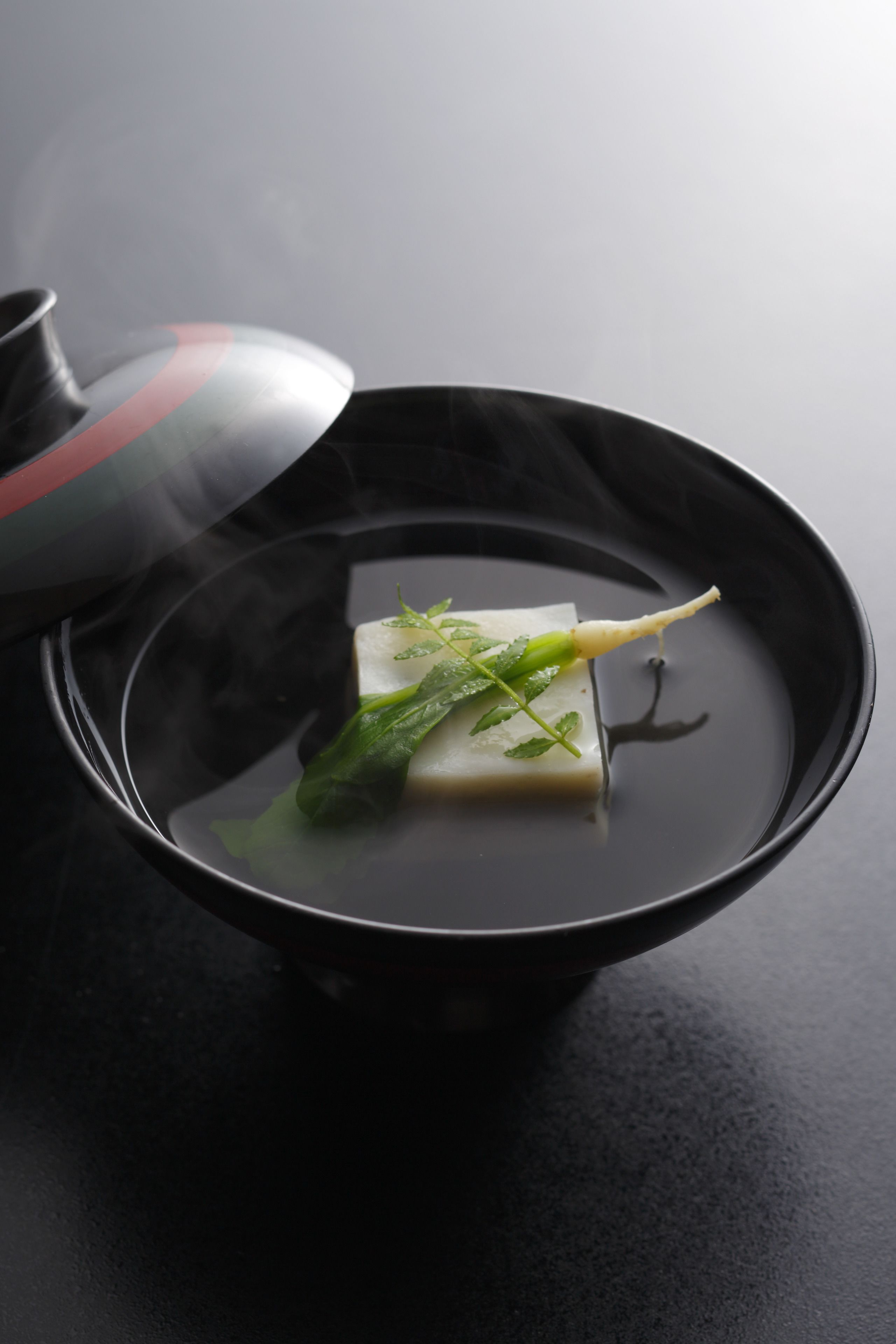 Un bol noir contenant un objet rectangulaire et des feuilles vertes dans un liquide, de la vapeur s'élevant du bol.