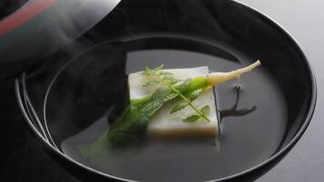 A black bowl with a rectangular object and green leaves in a liquid, steam rising from the bowl.