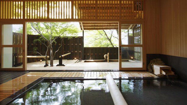 A traditional Japanese onsen with a wooden interior, a view of the outdoors, and a small wooden bench. - Negiya Ryofukaku (Kobe)