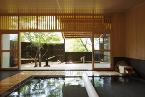 Un onsen japonés tradicional con interiores de madera, vistas al exterior y un pequeño banco de madera.