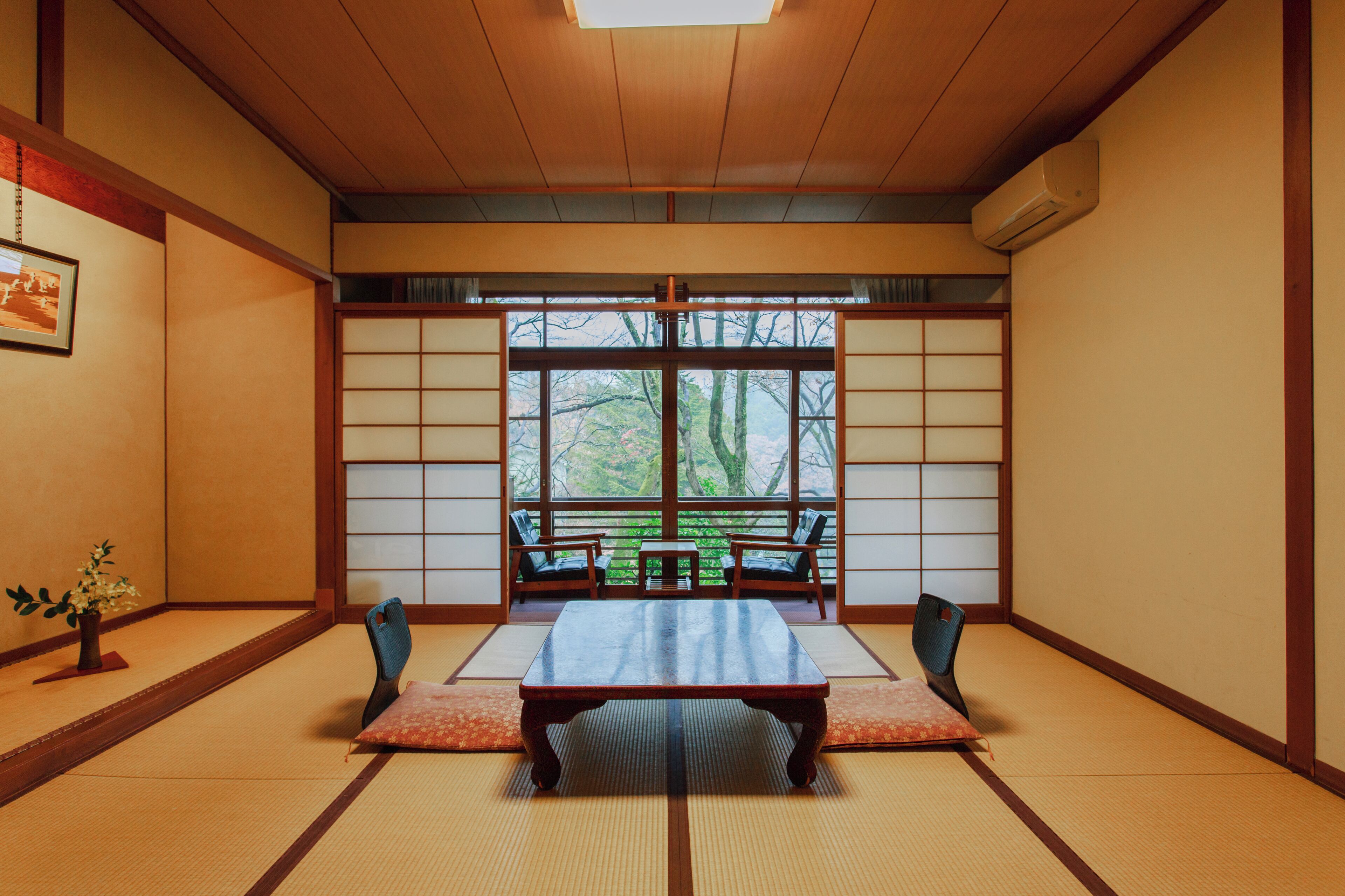 A traditional Japanese room with tatami flooring, a low table, and sliding doors leading to a view of trees.