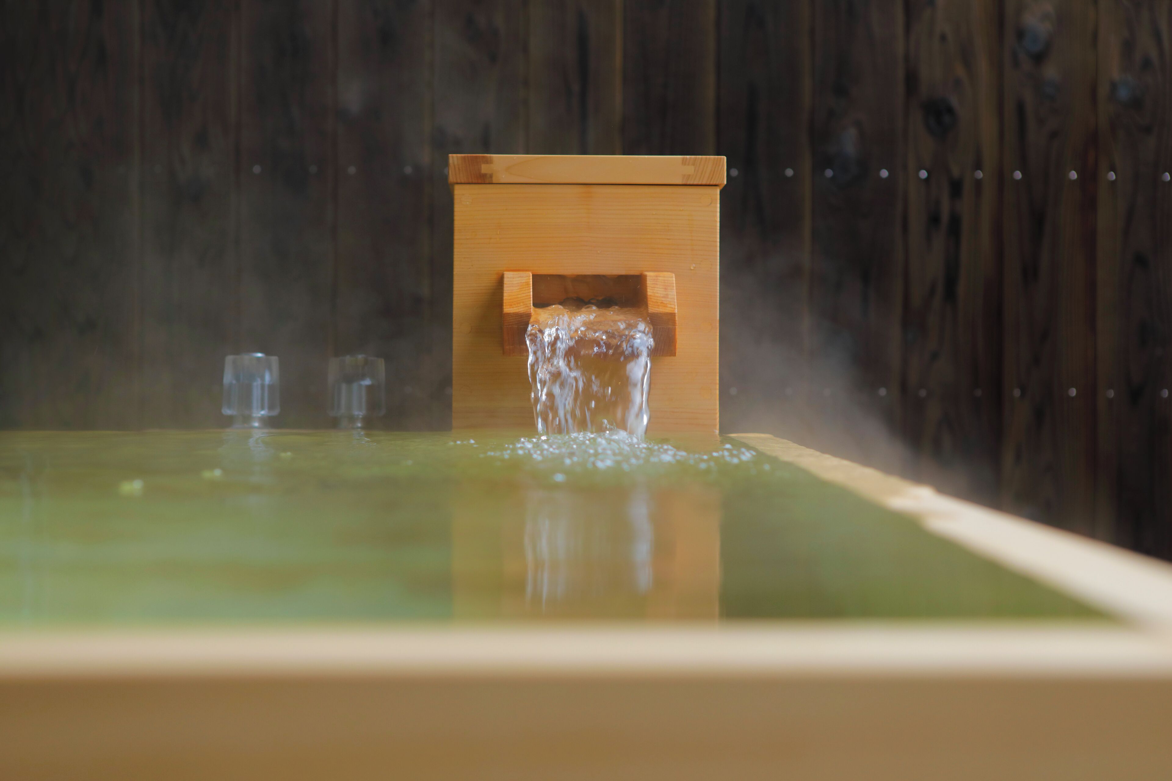 A wooden structure with a water spout, a reflective surface, and a wooden background.
