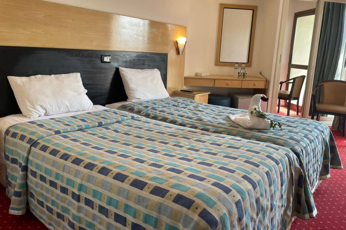 Une chambre d’hôtel avec deux lits, une tête de lit en bois, un bureau avec une chaise et un miroir au mur.