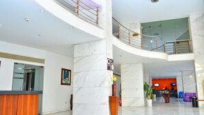 A spacious lobby with marble floors, a reception desk, a staircase, and a seating area.