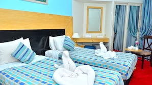 A hotel room with two beds, a wooden headboard, a desk with a lamp, a mirror, and a red carpet.