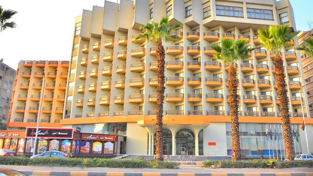 A multi-story hotel with balconies, palm trees, and a restaurant named "Milano" at the ground level.