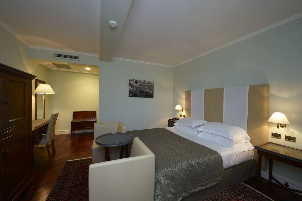 A hotel room with a bed, bedside tables, a desk, a chair, a lamp, and a picture on the wall.