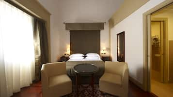 Ein Hotelzimmer mit einem Bett, zwei Nachttischen mit Lampen, einem runden Tisch, zwei Sesseln, einem gemusterten Teppich und einer Tür zu einem Badezimmer.