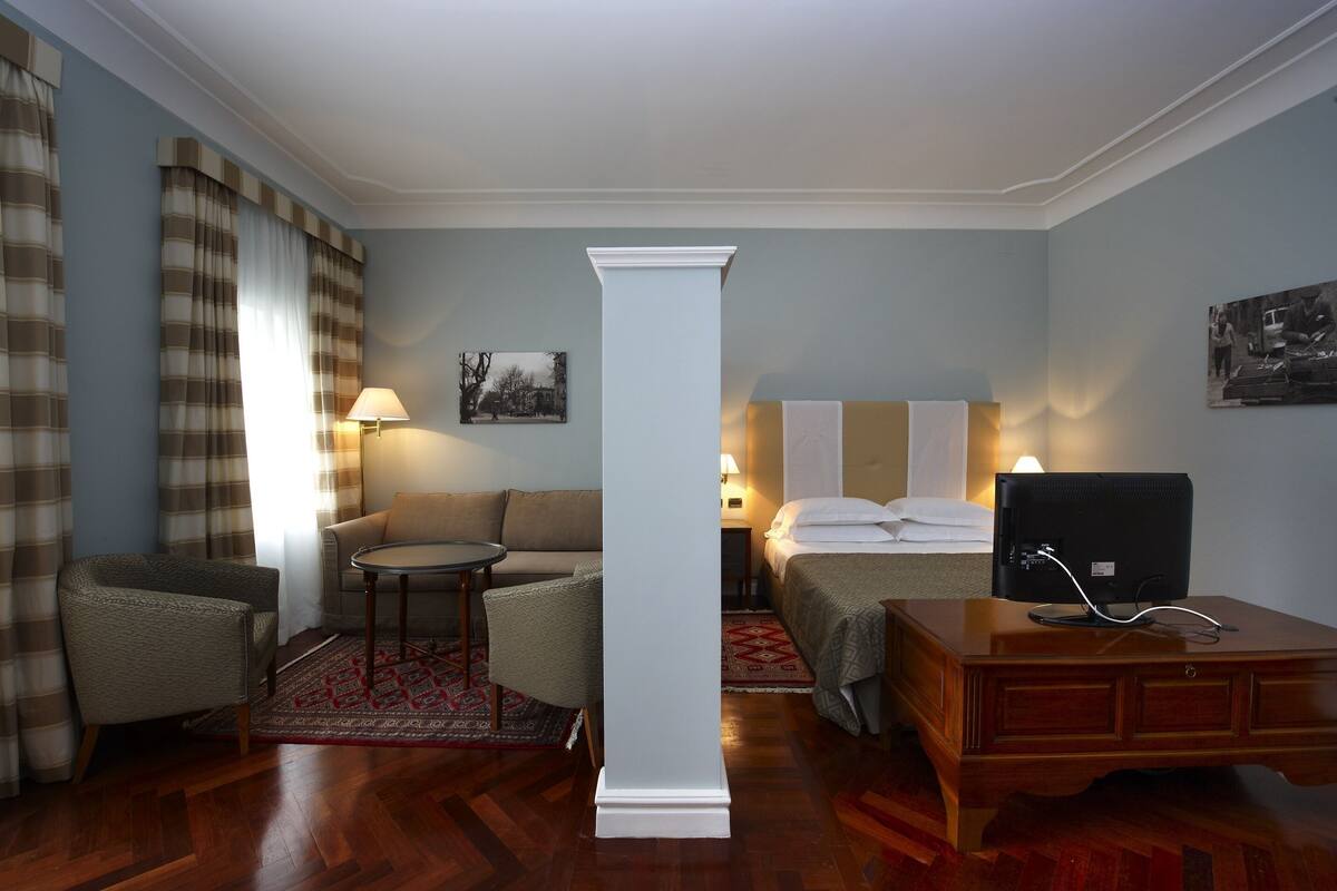 A hotel room with a bed, a desk, a chair, a sofa, a small table, and a lamp.