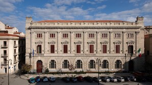 Ein historisches Gebäude mit einem zentralen Eingang, zahlreichen Fenstern und einer Flagge.
