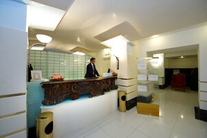 Un comptoir d’accueil avec un homme debout derrière, une poubelle et une chaise rouge à l’arrière-plan.
