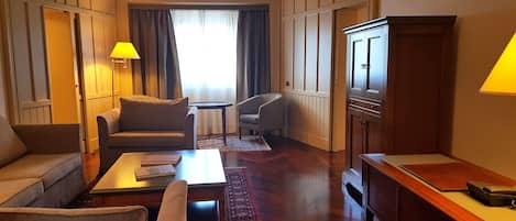 Ein Hotelzimmer mit einer Couch, einem Sessel, einem kleinen Tisch, einem Schrank und zwei Lampen.