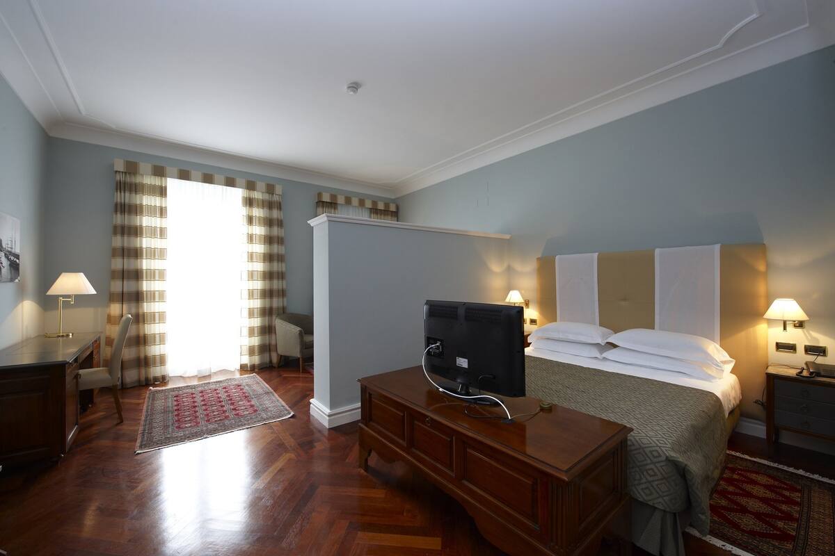 A hotel room with a bed, a desk, a TV, and a nightstand with lamps.