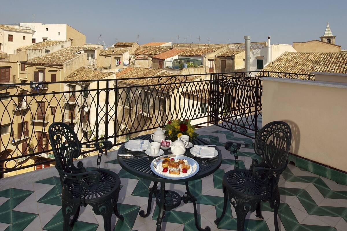 A terrace with a table set for two, surrounded by chairs, overlooking a cityscape.