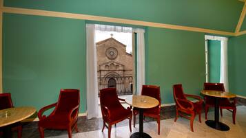 Un espace repas avec des chaises rouges et des tables rondes, une vue sur une église par la fenêtre et des murs verts.