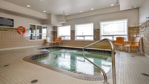 Una piscina interior con suelo de baldosas, un flotador y varias sillas alrededor de la zona de la piscina.