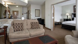 Habitación de hotel con sofá, una mesa de centro, cama, escritorio y un baño a la vista.