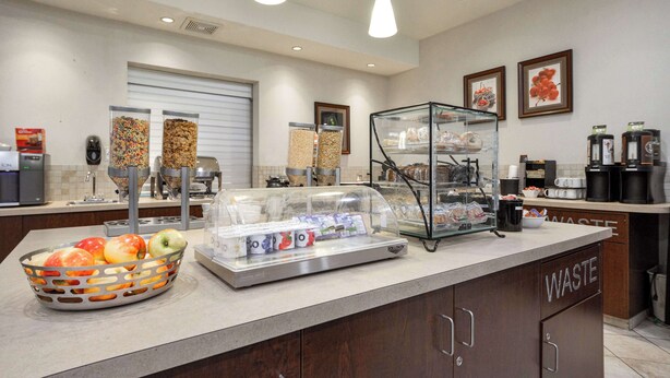 Una cocina de hotel con una cesta de fruta, un refrigerador expositor y un contenedor de basura.