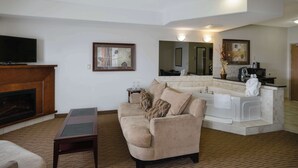 Una sala de estar con sofá, una mesa de centro, chimenea, televisor y una zona de cocina con lavamanos y encimera.