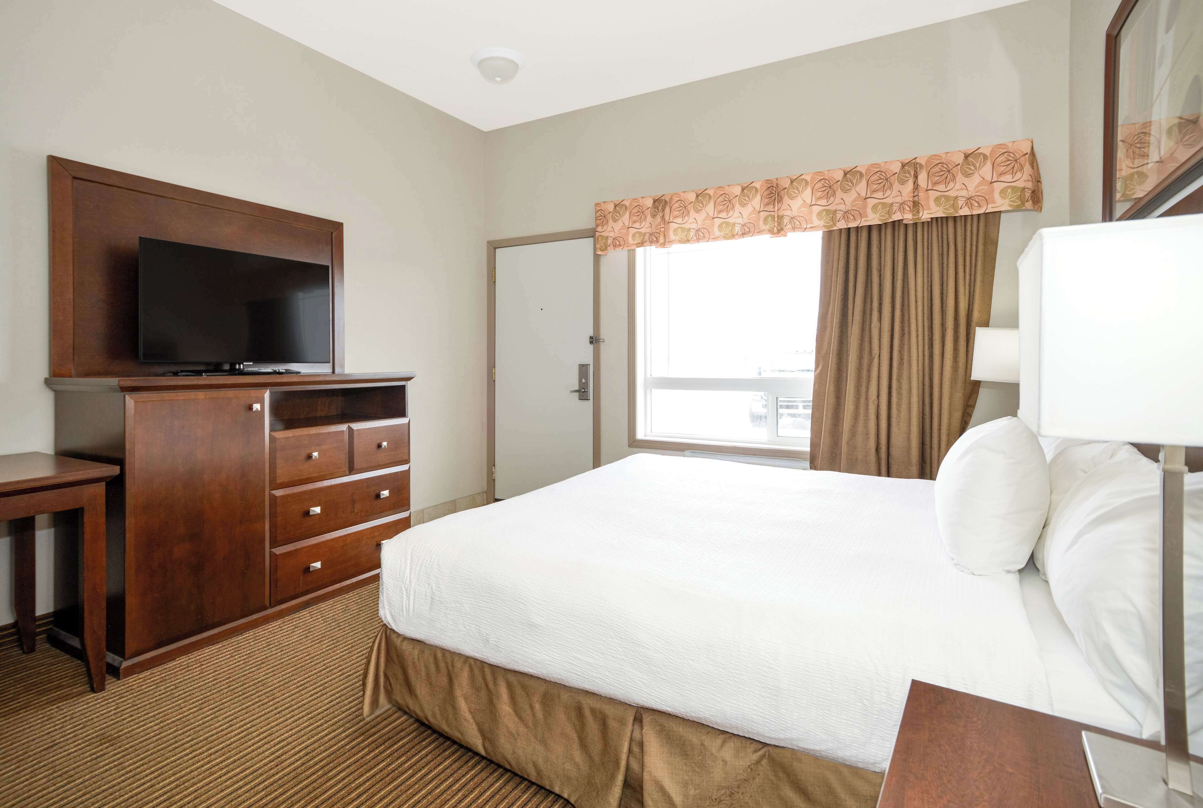 A hotel room with a bed, a TV on a wooden cabinet, a window with curtains, and a door.