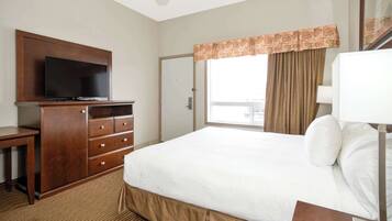 A hotel room with a bed, a TV on a wooden cabinet, a window with curtains, and a door.