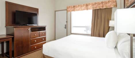 A hotel room with a bed, a TV on a wooden cabinet, a window with curtains, and a door.