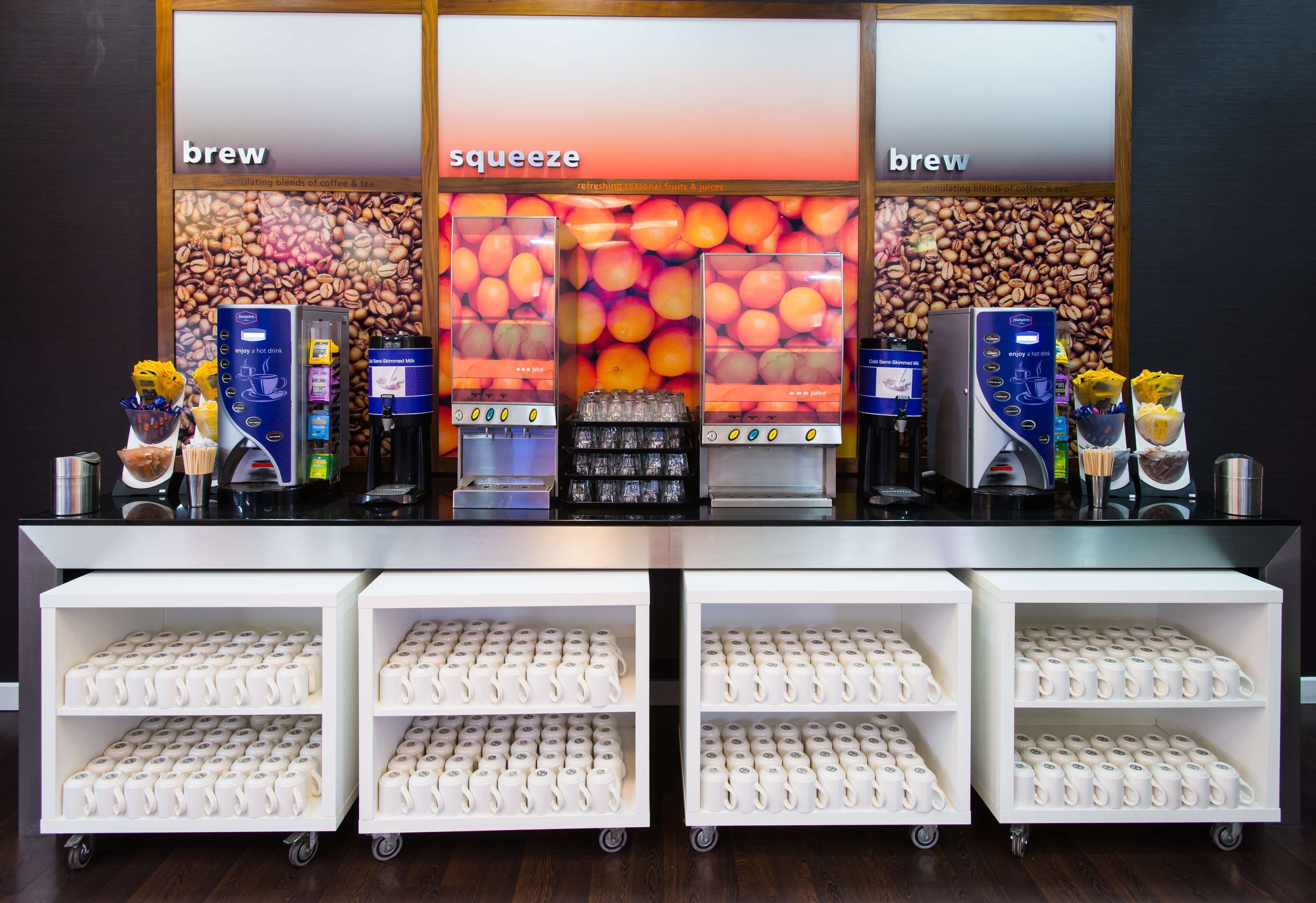 A coffee shop counter with labeled sections for 'brew' and 'squeeze' beverages, coffee machines, and a variety of coffee cups on shelves.