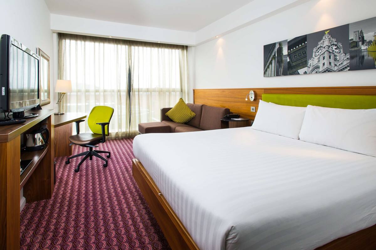 A hotel room with a large bed, a desk with a computer, a chair, and a television.