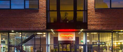 A hotel with a prominent Hampton sign, large windows, and a staircase leading to an upper level.