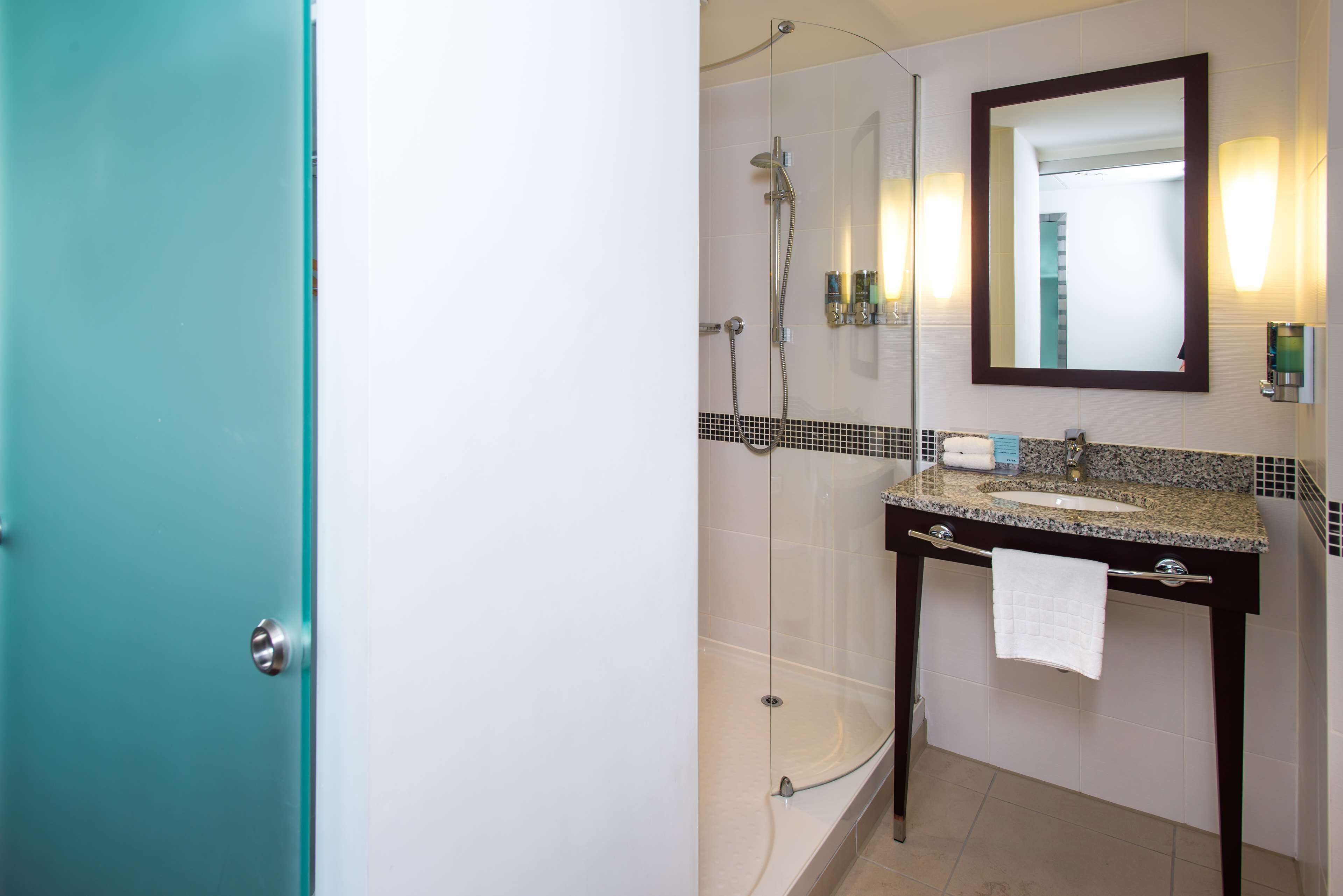 Un baño con cabina de ducha de vidrio, lavabo de encimera de granito y un espejo grande.