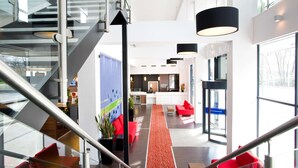 Un moderno vestíbulo de hotel con una escalera, un mostrador de recepción y un pasillo alfombrado en rojo.