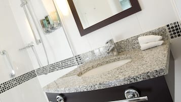 Un baño moderno con encimera de granito, un espejo grande y una lámpara fijada a la pared.