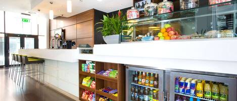 A modern hotel lobby with a snack bar, refrigerated beverage dispensers, and a seating area.