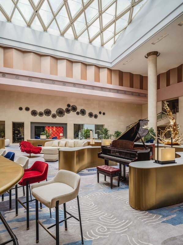 A spacious lobby with a grand piano, comfortable seating, and a high ceiling with natural light.