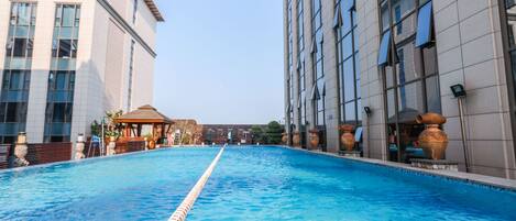 A swimming pool with clear blue water, surrounded by modern buildings with large windows and decorative vases.