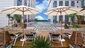 A poolside area with lounge chairs and umbrellas, surrounded by stone walls and potted plants. - Marco Polo Jinjiang (Quanzhou)