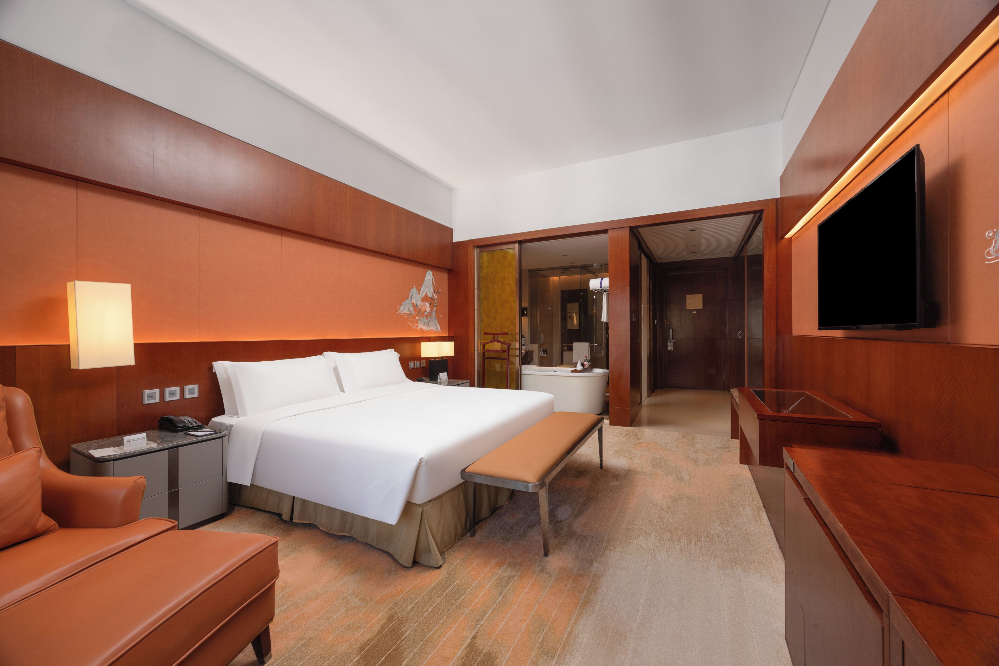 A hotel room with a bed, bedside table, lamp, chair, and a TV mounted on the wall.